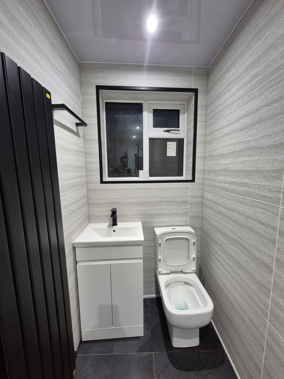 Grey tile bathroom with black vertical radiator